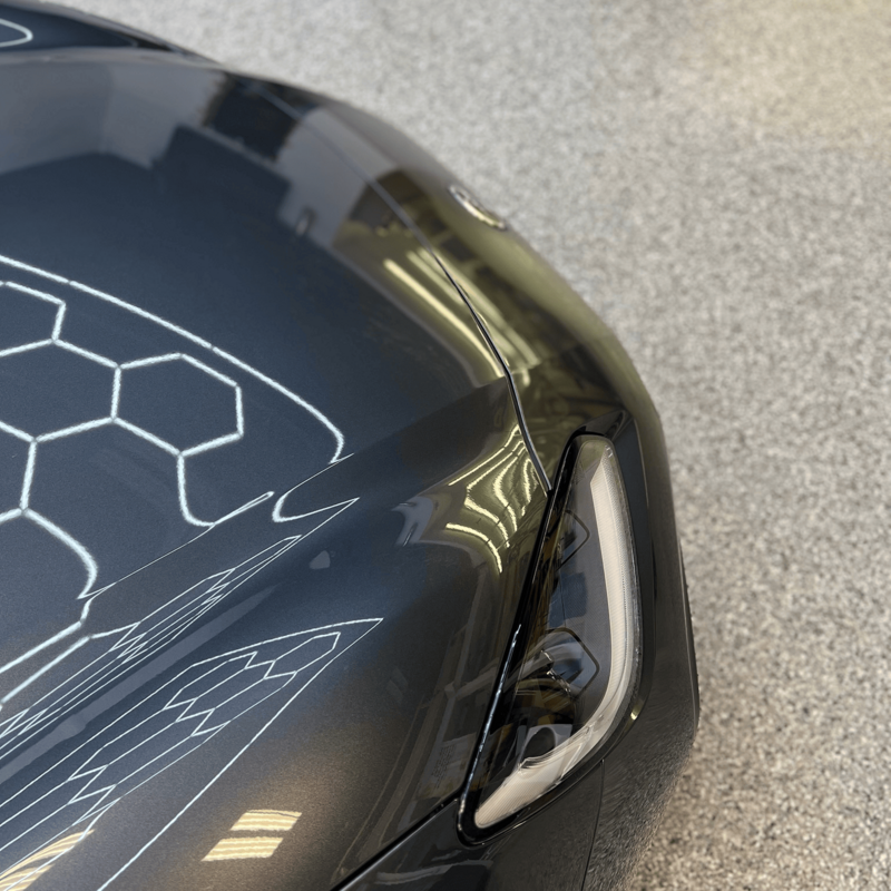 Reflection of studio lighting across a mirror-finish black hood after paint correction